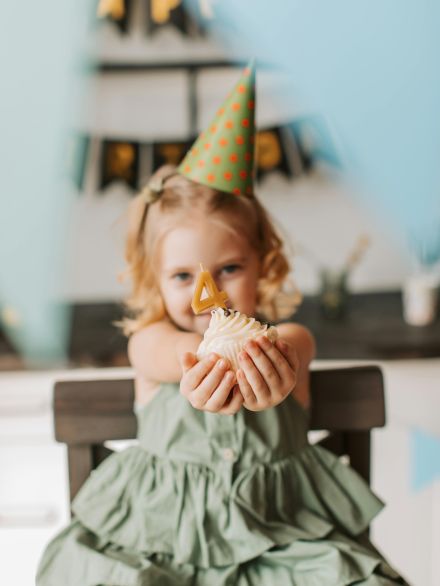 Little Girl with a Birthday Hat Holding a Cupcake with a Candle in a Shape of Number 4